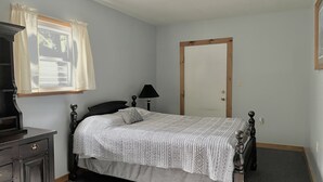 Un dormitorio con una cama individual, un aparador, una lámpara y una puerta.