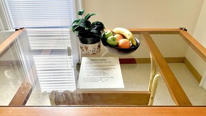 Una mesa con cubierta de vidrio, un frutero, una planta en maceta y un cartel de bienvenida con números de contacto de emergencia.