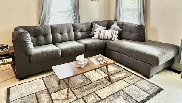 Una sala de estar con un sofá seccional gris, una mesa de centro de madera y una alfombra estampada.