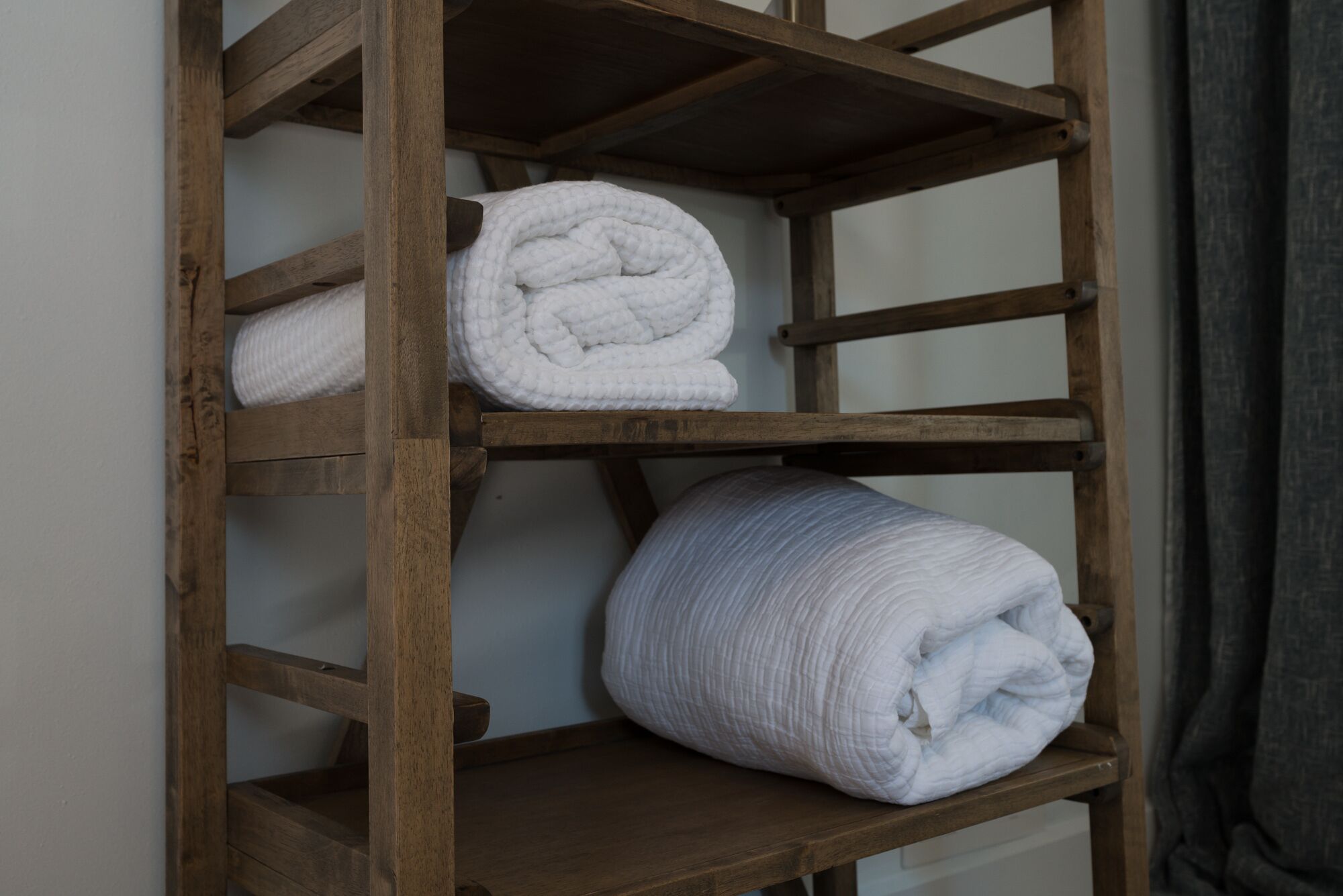A wooden shelf with three rolled white towels.