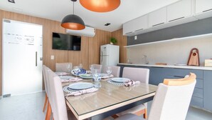 A modern kitchen with a built-in oven, a dining table set with plates and glasses, and a TV mounted on the wall. - Bauten 211 Cabo Branco por Carpediem (João Pessoa)