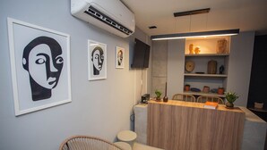 A modern reception area with a wooden counter, a mounted flat-screen TV, and wall-mounted air conditioning. - Bauten 211 Cabo Branco por Carpediem (João Pessoa)