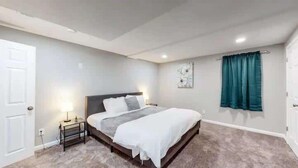 A bedroom with a bed, bedside table, wall art, and a window with curtains. - Spacious 6BR Home with Hot Tub, Hammocks and Firepit (Denver)
