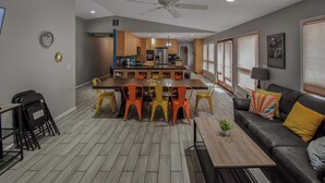 A modern kitchen with wooden cabinets, a central island, and a dining area with orange chairs. - Spacious 6BR Home with Hot Tub, Hammocks and Firepit (Denver)