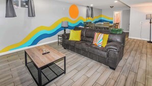 A living room with a sofa, a coffee table, and a wall mural. - Spacious 6BR Home with Hot Tub, Hammocks and Firepit (Denver)