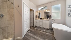 A modern bathroom with a walk-in shower, a freestanding bathtub, and a vanity with a large mirror and lights. - Brand new, 3 bedroom piece of  paradise! (Grand Junction)
