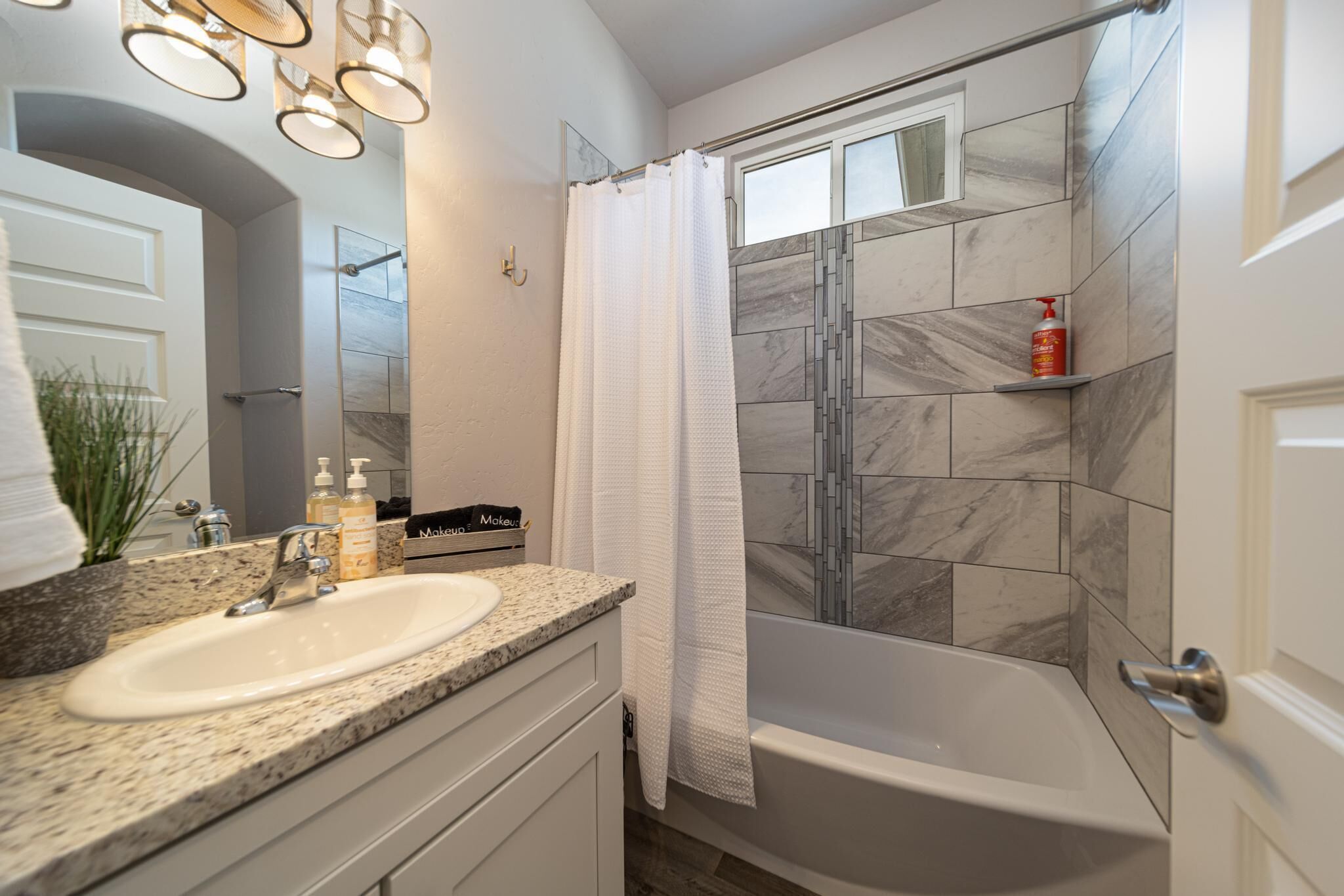 A bathroom with a white sink, granite countertop, a shower with a glass door, and a marble-tiled shower wall.