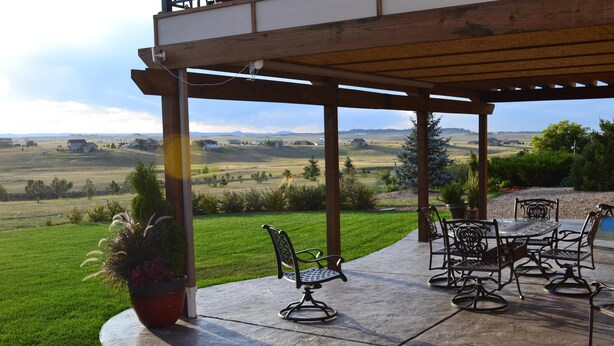 Un patio couvert avec des meubles d’extérieur, une plante en pot et une vue sur un paysage verdoyant.
