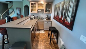 Une cuisine dotée d’un îlot central, un coin repas avec des chaises, un escalier et un grand tableau accroché au mur.
