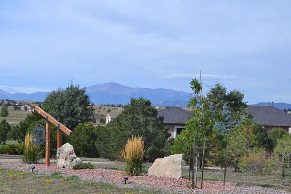 A residential area with a large rock, a wooden sign, and a house with a sloped roof.