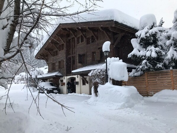 Un chalet en bois avec un toit en pente, entouré d’arbres couverts de neige et d’une clôture également recouverte de neige.