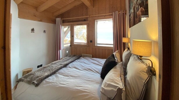 Ein Schlafzimmer mit Holzboden, einem Bett mit weißer Bettwäsche, einem Fellüberwurf und einem Nachttisch mit Lampe.