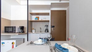 A compact kitchen with a microwave, coffee maker, and a refrigerator. There is a dining table set with plates, glasses, and cutlery. - Cabo Branco Bauten 207 por Carpediem (João Pessoa)