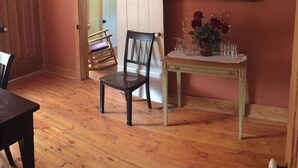 Ein Zimmer mit Holzboden, einem Holzsessel, einem Tisch mit Spitzenbettdecke und einem an der Wand befestigten Spiegel.