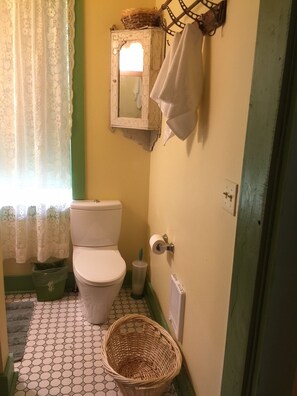 Une petite salle de bain comprenant des toilettes, un miroir, un porte-serviettes et un panier posé sur le sol.