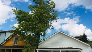 Ein weißes Holzhaus mit Veranda, einem Holzzaun und einem Baum davor.