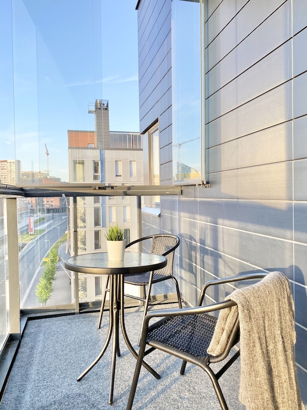 A balcony with a glass railing, a small round table with a potted plant, two wicker chairs, and a towel draped over a chair. - City Home Finland Ratina Panorama (Tampere)