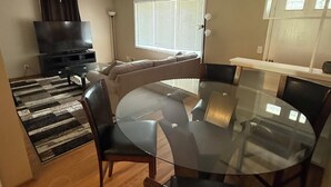 A modern living room with a glass dining table, leather chairs, a flat-screen TV, and a large window with blinds. - Cozy Ranch (Rochester)
