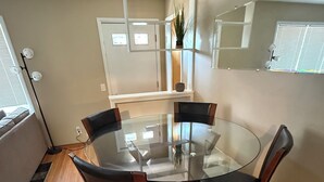 A dining area with a glass table surrounded by chairs, a floor lamp, and a window with blinds. - Cozy Ranch (Rochester)