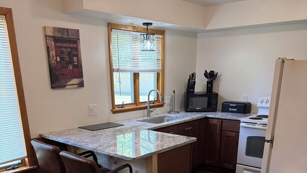 A kitchen with a granite countertop, wooden cabinets, a built-in oven, and a window with blinds. - Cozy Ranch (Rochester)
