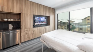A modern hotel room with a wooden cabinet, a built-in TV, a bed, and a view of the outside.