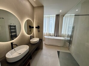 Un baño moderno con un lavamanos ovalado grande, una bañera independiente y un espejo amplio con iluminación integrada.