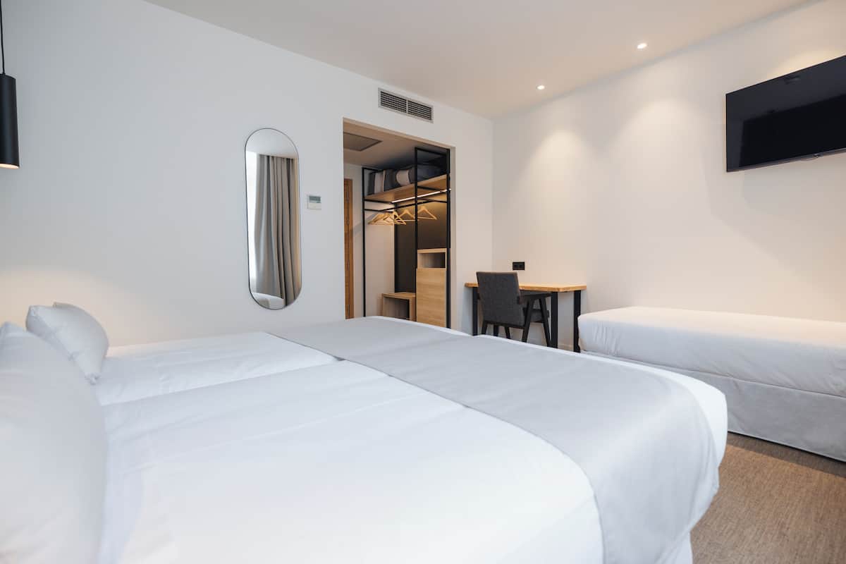 A hotel room with two single beds, a desk, a chair, a TV, and a walk-in closet.