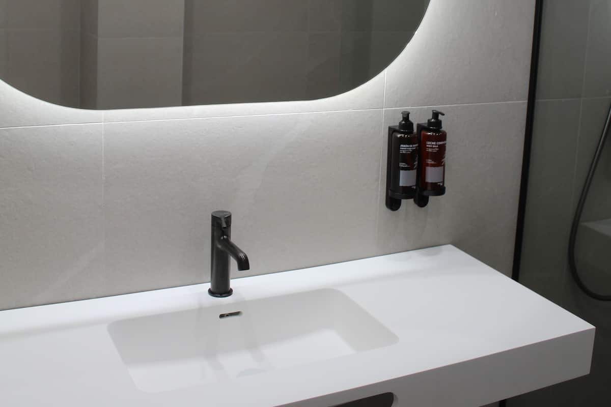 A modern bathroom with a white sink, a large mirror, and two bottles of shampoo on the wall.
