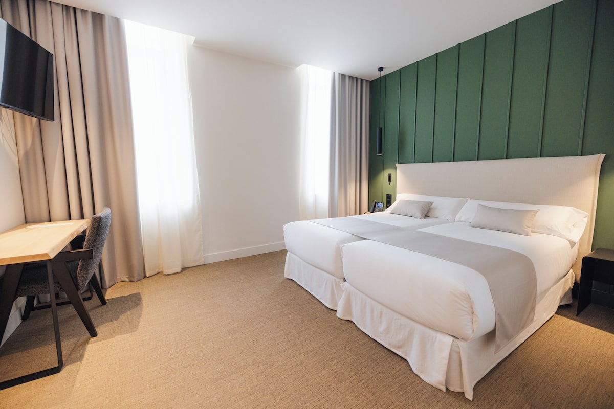 A hotel room with a large bed, a desk, and a TV mounted on the wall.
