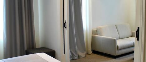 Una habitación de hotel con una cama grande, un área de descanso pequeña y una puerta que conduce a otra habitación.