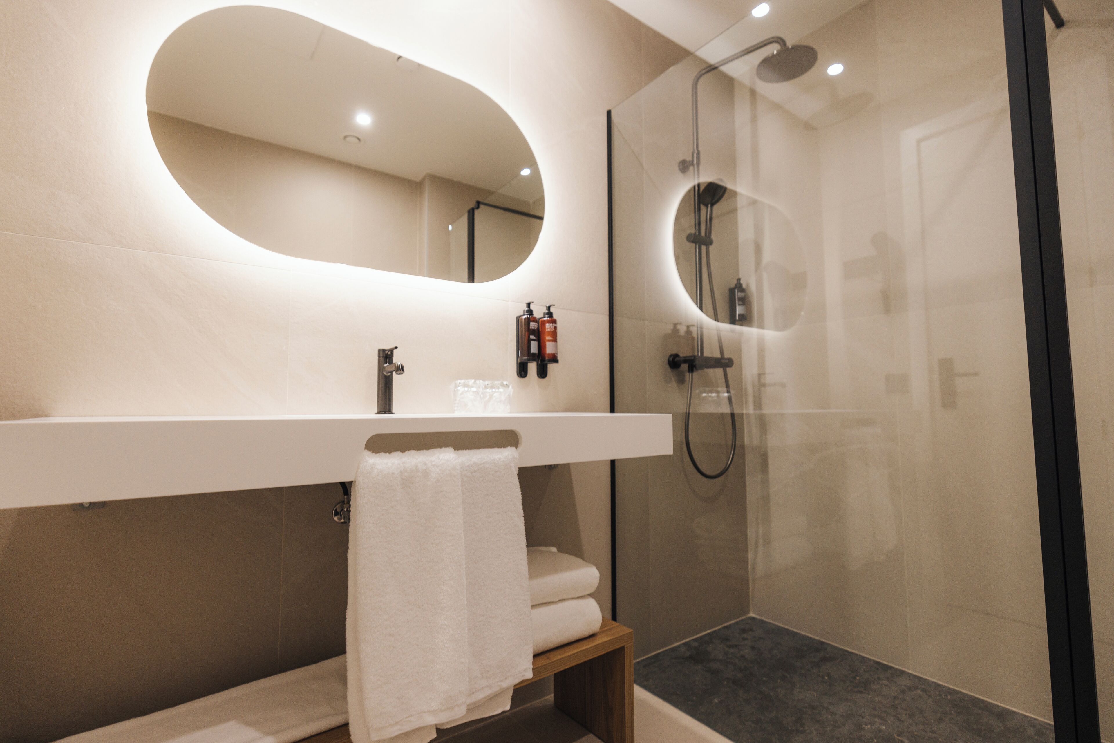 A modern bathroom with a large mirror, a shower, and a vanity with a towel.