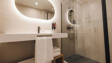 A modern bathroom with a large mirror, a shower, and a vanity with a towel.