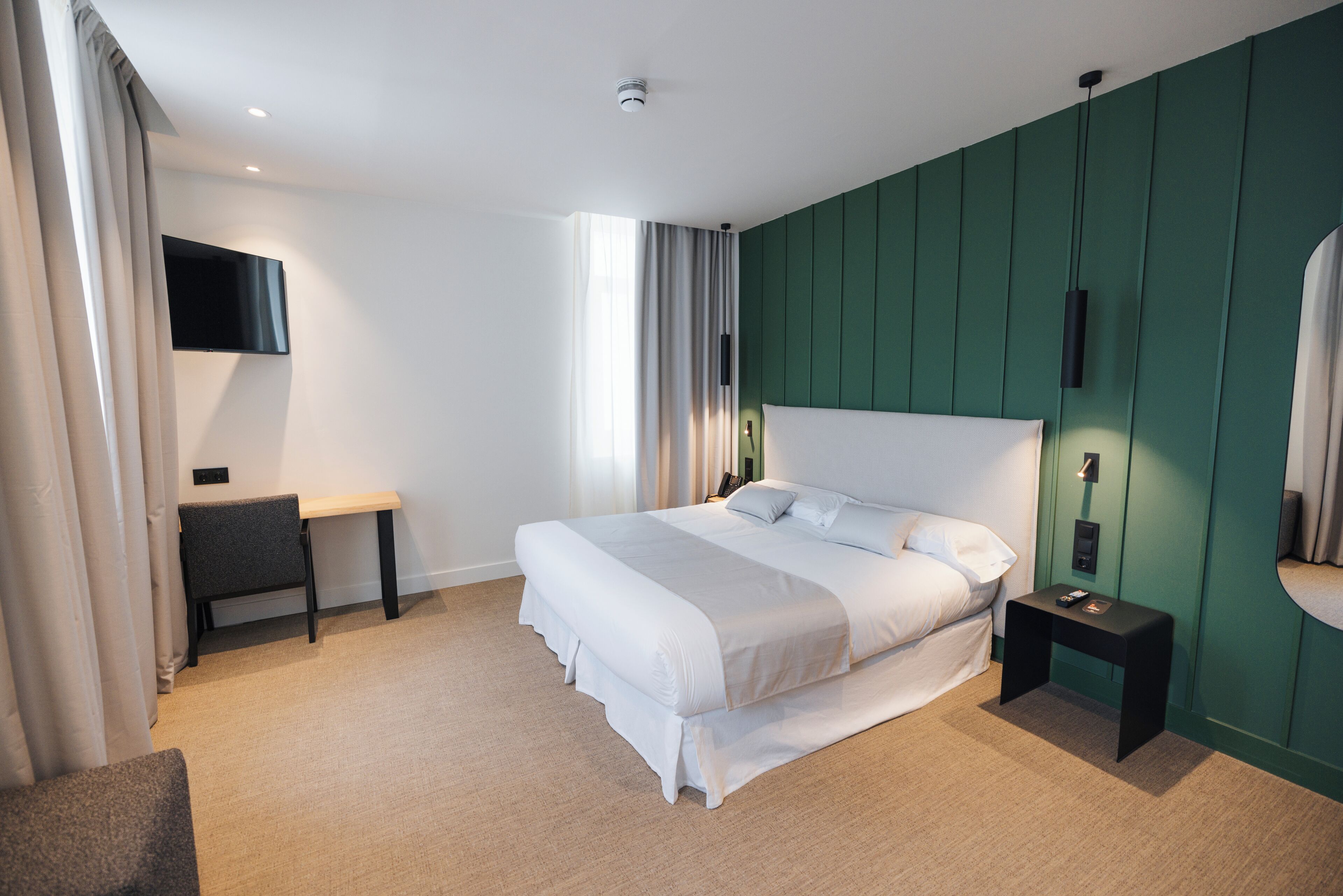 Une chambre d’hôtel moderne dotée d’un grand lit, d’un bureau, d’une télévision à écran plat et d’un mur d’accent de couleur verte.