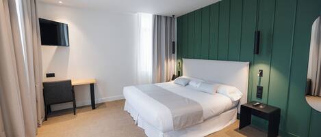 A modern hotel room with a large bed, a desk, a flat-screen TV, and a green accent wall.