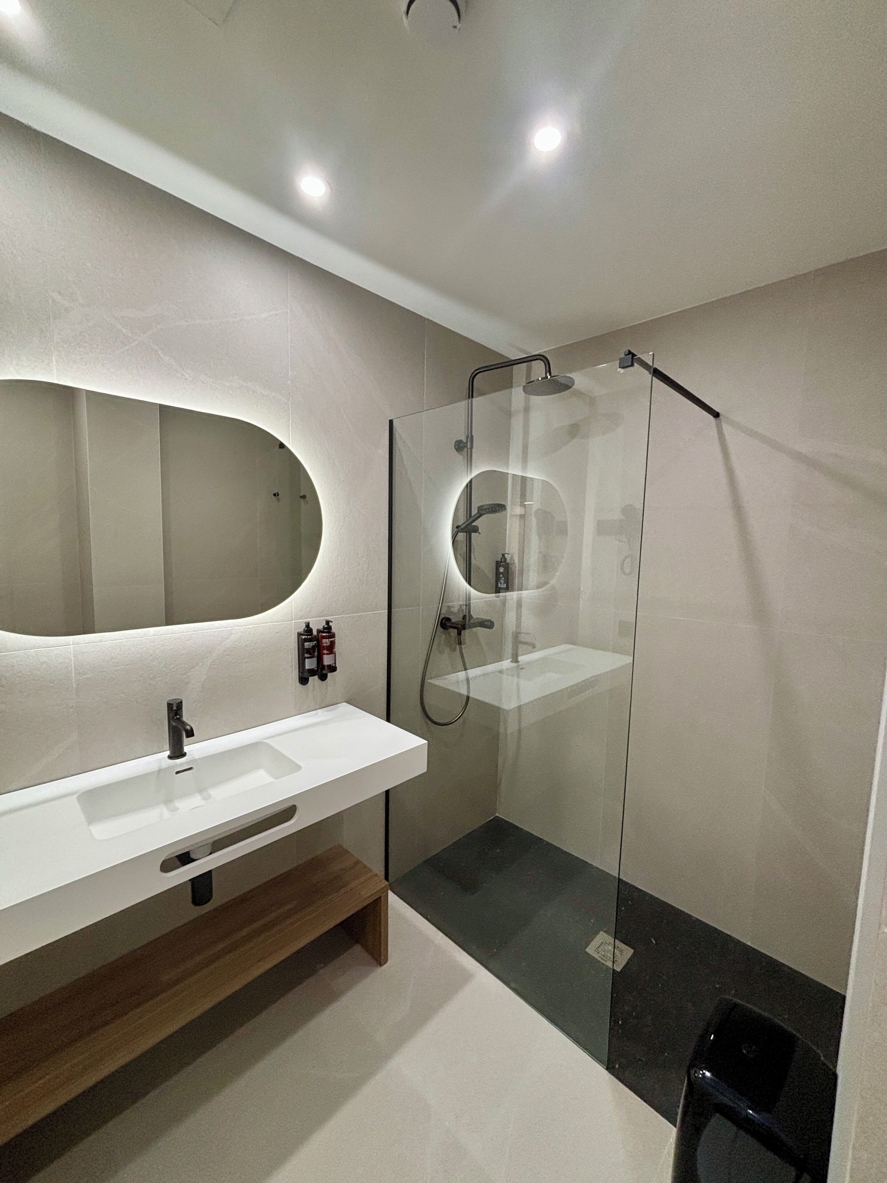 Un baño moderno con un espejo grande, un lavabo blanco y una zona de ducha con mampara de cristal.