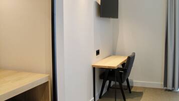 A modern hotel room with a wooden desk, a flat-screen TV mounted on the wall, and a comfortable chair.
