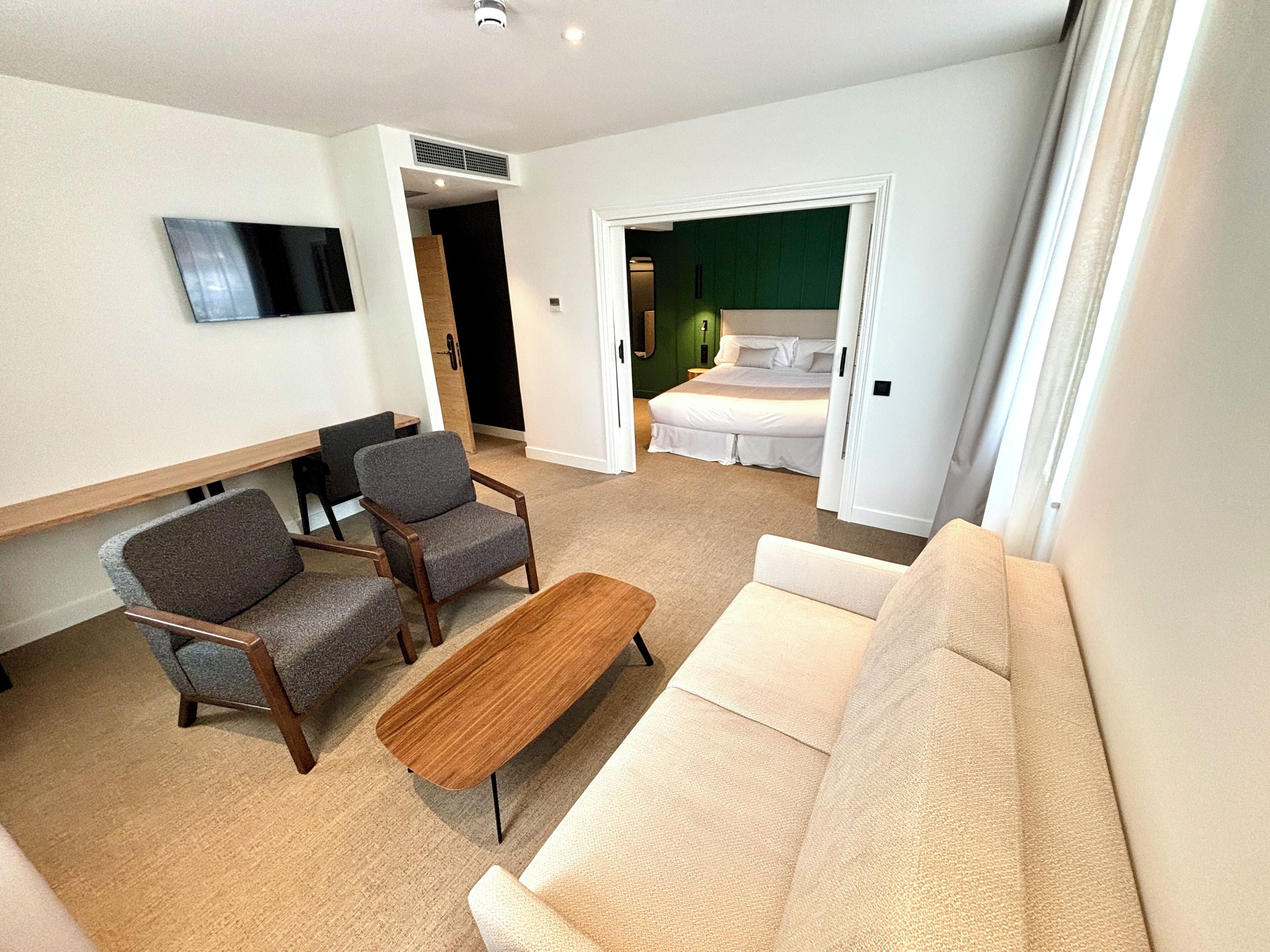 A modern living room with a sofa, two armchairs, a coffee table, and a flat-screen TV mounted on the wall.