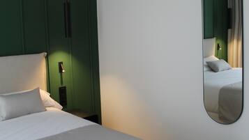 Ein ordentlich bezogenes Bett mit weißen Bettwäsche, eine grüne Akzentwand und ein großer Spiegel, der den Raum widerspiegelt.