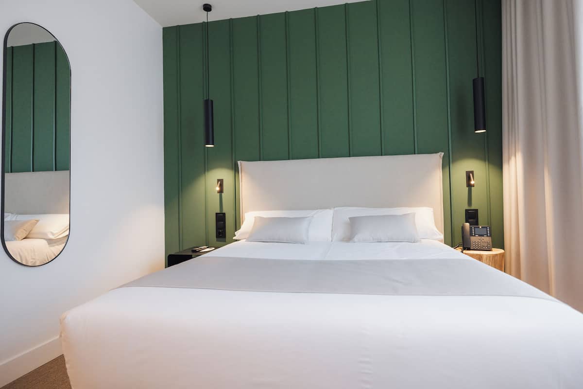 A modern hotel room with a large bed, green paneling on the walls, and a bedside telephone.