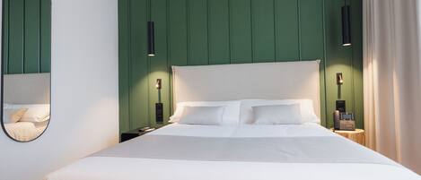 A modern hotel room with a large bed, green paneling on the walls, and a bedside telephone.