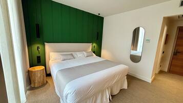 A neatly made bed with white linens in a room with green paneling on the walls and a large mirror on the wall.