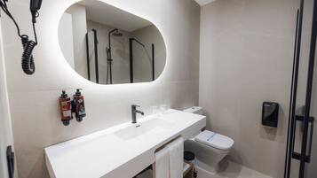 Een moderne badkamer met een wit wastafelmeubel, een grote spiegel, een toilet en een douche.