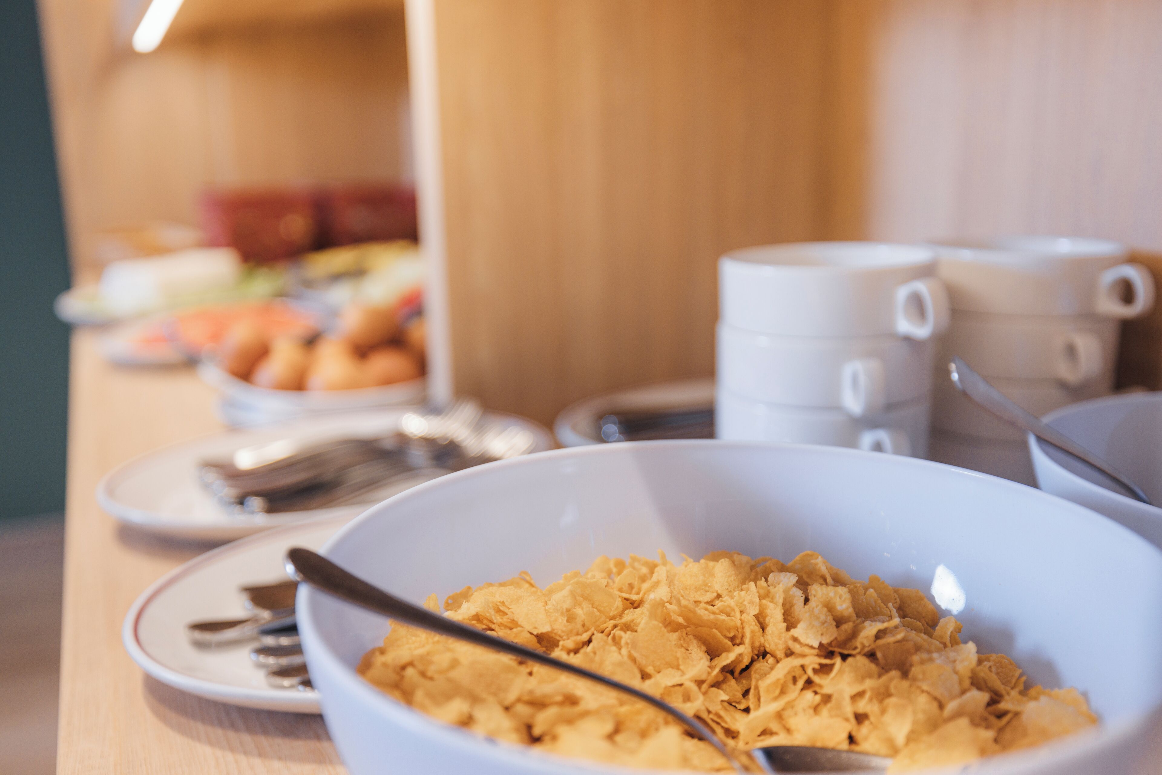 A breakfast buffet with cereal, coffee cups, and utensils.