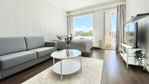 Ein modernes Wohnzimmer mit einem grauen Sofa, einem runden weißen Couchtisch und einem Flachbildfernseher auf einem weißen Schrank.