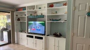 A living room with a television on a white entertainment unit, shelves with decorative items, and a door to the right. - Crystal River Condo -Near Three Sisters and Hunters Spring (Crystal River)