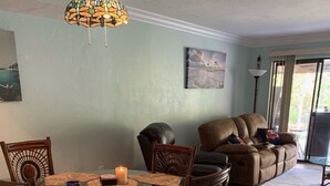A dining area with a round glass table, wicker chairs, and a hanging light fixture. - Crystal River Condo -Near Three Sisters and Hunters Spring (Crystal River)