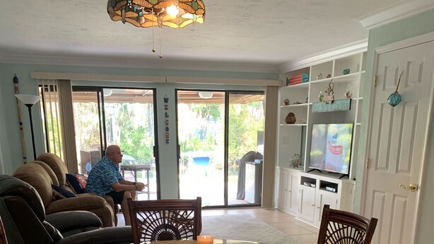 A dining area with a glass table surrounded by wicker chairs, a chandelier above, and a television in the background. - Crystal River Condo -Near Three Sisters and Hunters Spring (Crystal River)