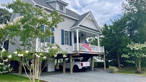 Une grande maison avec un porche couvert, un drapeau et un camion garé devant.