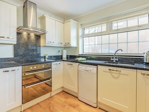 A modern kitchen with white cabinets, a stainless steel range hood, a built-in oven, a dishwasher, and a window above the sink. - Spacious property and stunning sea views in great location. (Greatstone)
