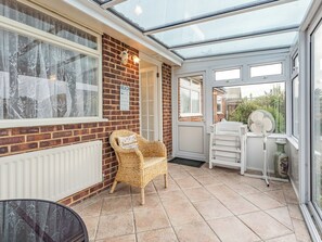 Een orangerie met een rieten stoel, een witte radiator en een ventilator.